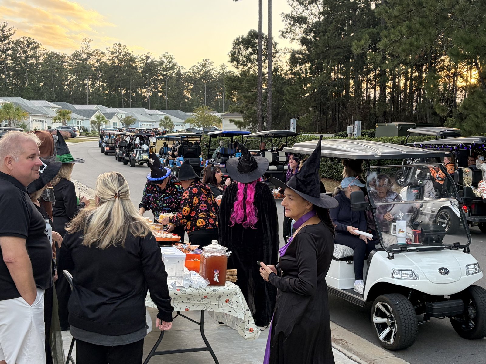 Golf cart pulling up to a table with a drink dispenser and treats, surrounded by people in witch costumes